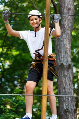 Orman macera parkı çocuk. Çocuk turuncu kask ve mavi t gömlek tırmanıyor yüksek ip izinde. Çeviklik beceri ve açık hava eğlence merkezi çocuklar için tırmanma. Genç çocuk açık havada çalış