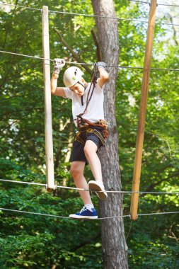 Orman macera parkı çocuk. Çocuk turuncu kask ve mavi t gömlek tırmanıyor yüksek ip izinde. Çeviklik beceri ve açık hava eğlence merkezi çocuklar için tırmanma. Genç çocuk açık havada çalış