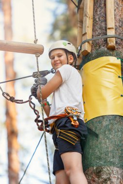 Orman macera parkı çocuk. Çocuk turuncu kask ve mavi t gömlek tırmanıyor yüksek ip izinde. Çeviklik beceri ve açık hava eğlence merkezi çocuklar için tırmanma. Genç çocuk açık havada çalış