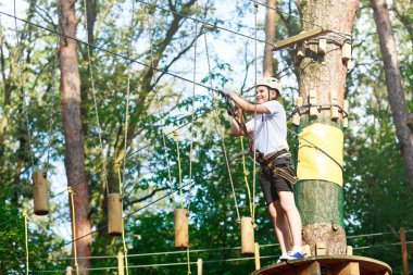 Orman macera parkı çocuk. Çocuk turuncu kask ve mavi t gömlek tırmanıyor yüksek ip izinde. Çeviklik beceri ve açık hava eğlence merkezi çocuklar için tırmanma. Genç çocuk açık havada çalış