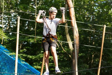 Sevimli çocuk macera parkı güneşli yaz gününde tırmanma etkinliğini zevk. İp Bahçesi yapısında tırmanma çocuk. Kask sigorta ile tırmanma güvenli. Çocuk orman macera parkı, aşırı spor