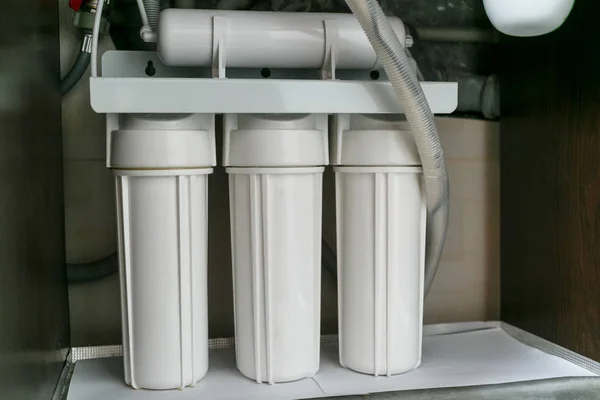 Reverse osmosis water purification system at home. Installation of water purification filters under kitchen sink in cupboard. Clear water concept