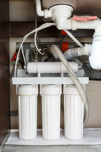 Reverse osmosis water purification system at home. Installation of water purification filters under kitchen sink in cupboard. Clear water concept