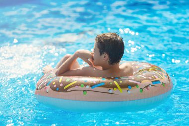 Cute sporty boy swims in the pool with donut ring and has fun. Vacation with kids, holidays, active weekends, summer concept. Chocolate donut