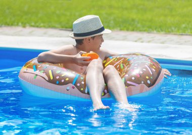 Şirin çocuk çocuk komik şişme çörek float halkası portakal ile yüzme havuzunda üzerinde. Yüzmeyi, öğrenme genç Resort'ta açık yüzme havuzunda eğlenceli var. Su oyuncaklar çocuklar için. Sağlıklı spor aktivitesi, tatil 