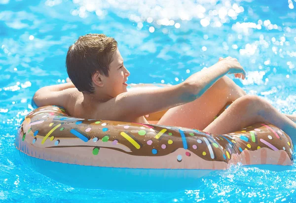 Happy cute little boy teenager lying on  inflatable donut ring  in swimming pool.  Active games on water, vacation, holidays concept. Chocolate donut. Cool fun summer holidays for children.
