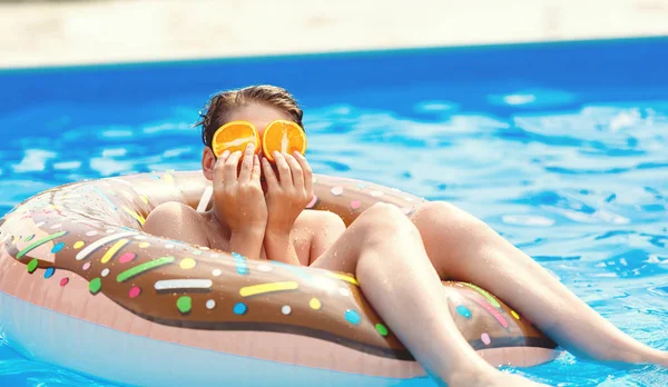 Cute child boy on funny inflatable donut float ring in swimming pool with oranges. Teenager learning to swim, have fun in outdoor pool at resort. Water toys for kids. Healthy sport activity, vacation