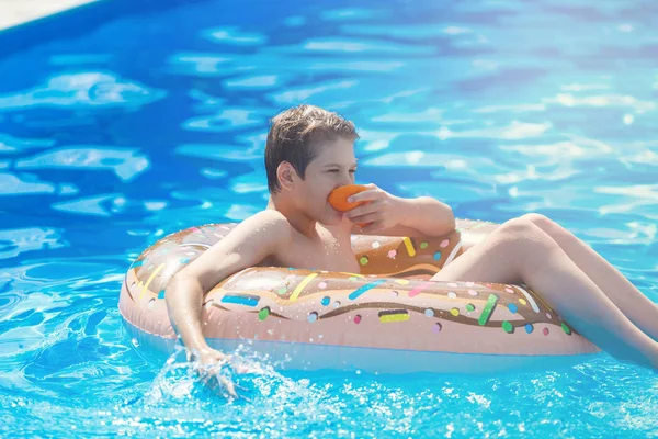 Şirin çocuk çocuk komik şişme çörek float halkası portakal ile yüzme havuzunda üzerinde. Yüzmeyi, öğrenme genç Resort'ta açık yüzme havuzunda eğlenceli var. Su oyuncaklar çocuklar için. Sağlıklı spor aktivitesi, tatil 