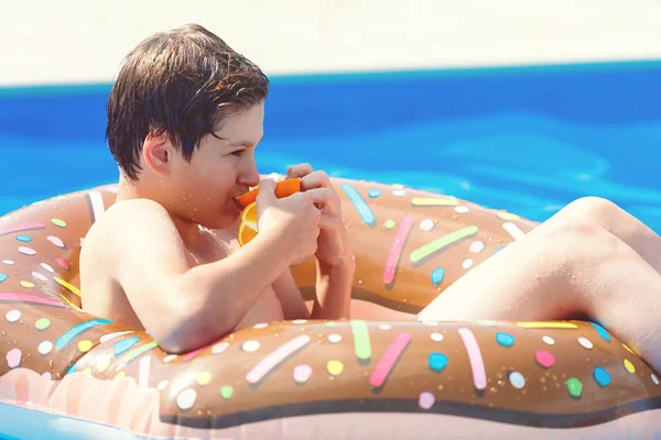 Cute child boy on funny inflatable donut float ring in swimming pool with oranges. Teenager learning to swim, has fun in outdoor pool at resort. Water toys for kids. Healthy sport activity, vacation 