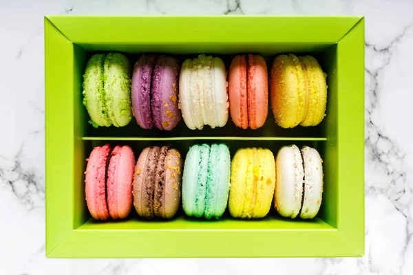 Green Box with colorful macarons and coffe cup on marble table background. Delicious sweets and coffee break