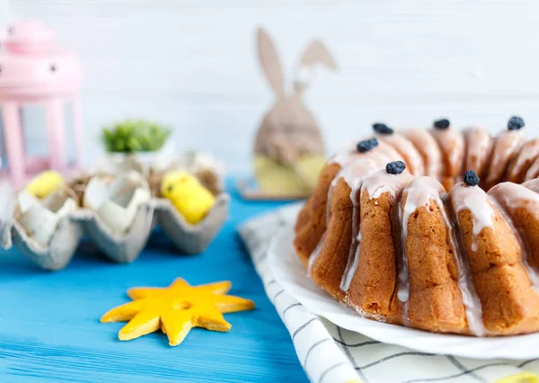 Happy Easter! Handmade cake on towel, eggs, wooden bunny rabit on blue wooden background. Decoration for Easter holiday