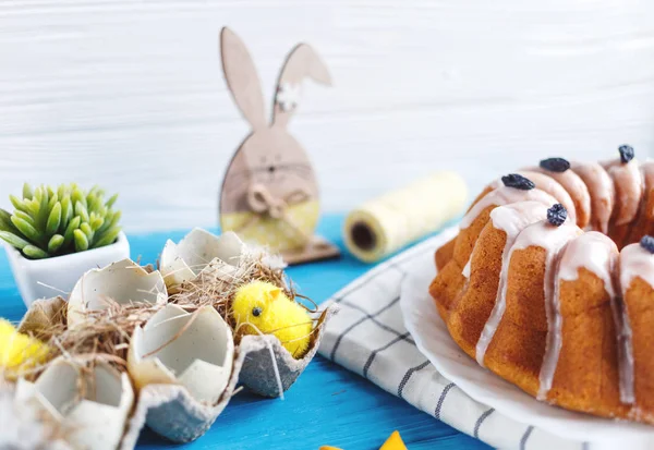 Happy Easter! Handmade cake on towel, eggs, wooden bunny rabit on blue wooden background. Decoration for Easter holiday