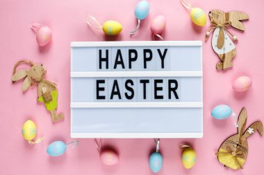 Mutlu paskalya metin pembe pastel kağıt sarı zemin üzerine lightbox üzerinde pembe, mavi yumurtaları ve bunnies. Paskalya, üstten görünüm, düz parlak şablon yatıyordu, tatil arka plan kopya alanı ile 