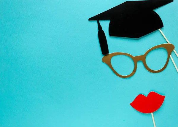 Creative background with photobooth props for graduation: hats, diploma, glasses, lips on bright blue paper background. Education, study concept.
