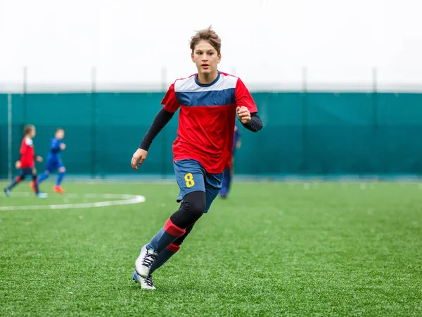 Kırmızı beyaz spor futbol sahası üzerinde çalışan çocuklar. Genç futbolcular top sürmek ve oyunda futbol topu tekmelemek. Eğitim, aktif yaşam tarzı, spor, çocuk etkinlik kavramı 