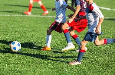 Kırmızı beyaz spor futbol sahası üzerinde çalışan çocuklar. Genç futbolcular top sürmek ve oyunda futbol topu tekmelemek. Eğitim, aktif yaşam tarzı, spor, çocuk etkinlik kavramı 