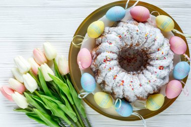 Mutlu Paskalya! Altın tepsi plaka ile kek ve el boyalı renkli yumurta, lale beyaz ahşap masa üzerinde. Kapat şunu. Paskalya için dekorasyon, şenlikli arka plan.