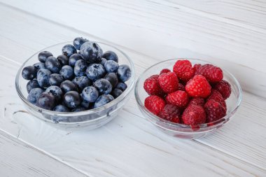 Beyaz ahşap masada ahududu yaban mersini ile küçük cam plakalar. Sağlıklı yemek, yaz meyveleri.