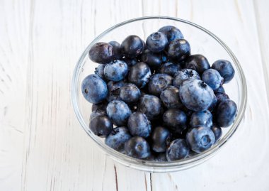 Beyaz ahşap masada yaban mersini ile küçük cam plaka. Sağlıklı yemek, yaz meyveleri.