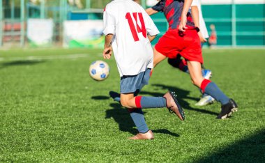 Kırmızı beyaz spor futbol sahası üzerinde çalışan çocuklar. Genç futbolcular top sürmek ve oyunda futbol topu tekmelemek. Eğitim, aktif yaşam tarzı, spor, çocuk etkinlik kavramı 