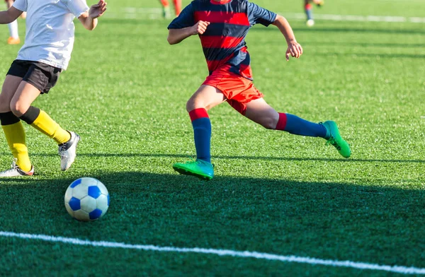 Boys in red white sportswear running on soccer field. Young footballers dribble and kick football ball in game. Training, active lifestyle, sport, children activity concept