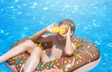 Yüzme havuzunda mutlu sevimli küçük çocuk genç. Aktif oyunlar su, tatil, tatil konsepti. Çikolatalı çörek. Çocuklar için serin eğlenceli yaz tatili.