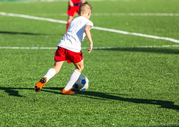 Boys in red white sportswear running on soccer field. Young footballers dribble and kick football ball in game. Training, active lifestyle, sport, children activity concept