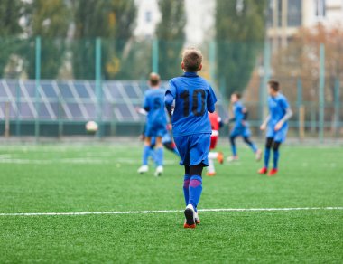Genç futbolcular maça ve Kick futbol topu oyunda. Futbol sahasında çalışan kırmızı mavi spor kıyafetine sahip çocuklar. Eğitim, aktif yaşam tarzı, spor, çocuk aktivite konsepti