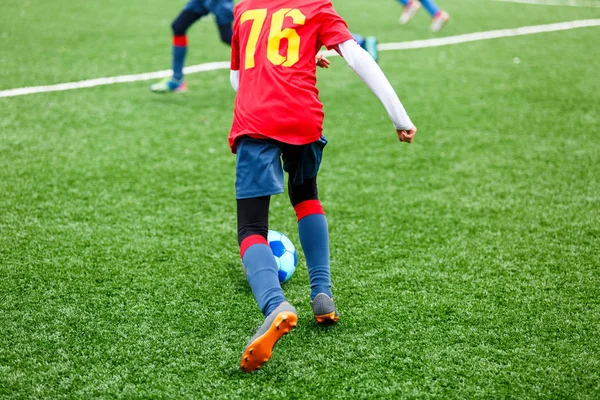 Young footballers dribble and kick football ball in game. Boys in red  blue sportswear running on soccer field. Training, active lifestyle, sport, children activity concept