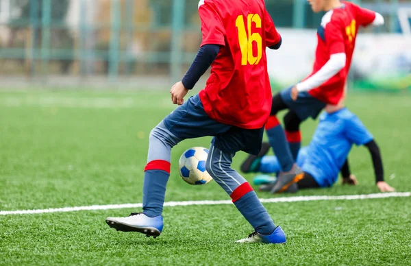 Young footballers dribble and kick football ball in game. Boys in red  blue sportswear running on soccer field. Training, active lifestyle, sport, children activity concept
