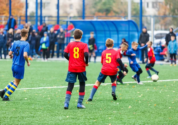 ゲームの若いサッカー選手ドリブルとキックフットボールボール レッドブルーのスポーツウェアの男子がサッカー場で走っている トレーニング アクティブなライフスタイル スポーツ 子供の活動の概念 — ストック写真