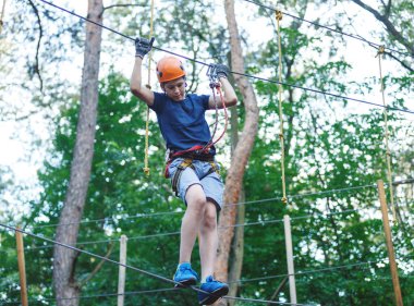 Beyaz tişörtlü sportif, genç, sevimli çocuk macera halat Parkı kask içinde ve yaz aylarında parktaki güvenli donanımları zamanını geçiriyor. Aktif yaşam tarzı kavramı