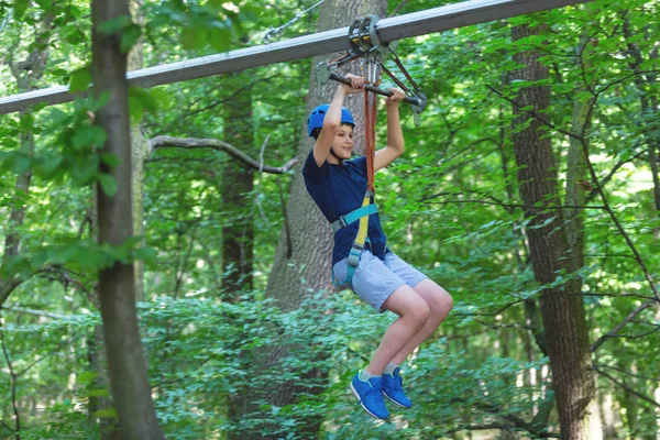 Beyaz tişörtlü sportif, genç, sevimli çocuk macera halat Parkı kask içinde ve yaz aylarında parktaki güvenli donanımları zamanını geçiriyor. Aktif yaşam tarzı kavramı