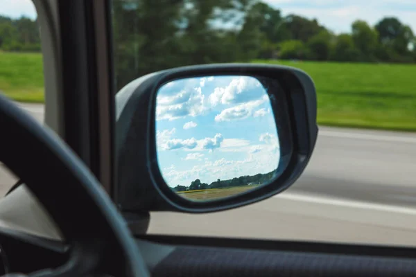 Reflection of blue sky with clouds in the mirror of a riding car in sunny day on the road.