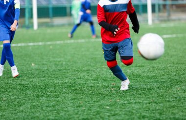 Kırmızı ve mavi spor giyen çocuklar sahada futbol oynar, top top akıtır. Yeşil çimüzerinde topu ile genç futbolcular. Eğitim, futbol, çocuklar için aktif yaşam tarzı 