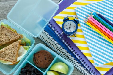 Ev yapımı sandviç, yeşil elma, kurabiyeler, kalemler, saat, masanın üzerinde defterler ile Okul mavi öğle yemeği kutusu. Okulda sağlıklı beslenme. Okul geçmişine geri dönelim. Düz döşeme, üst görünüm.