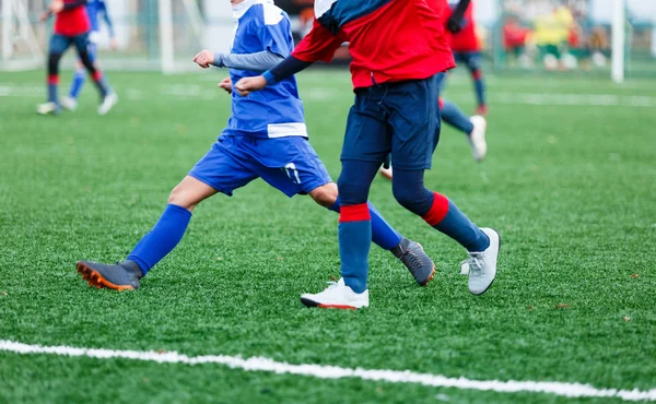 Boys in red and blue sportswear plays  football on field, dribbles ball. Young soccer players with ball on green grass. Training, football, active lifestyle for kids