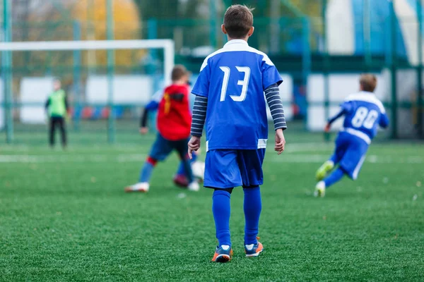 Kırmızı ve mavi spor giyen çocuklar sahada futbol oynar, top top akıtır. Yeşil çimüzerinde topu ile genç futbolcular. Eğitim, futbol, çocuklar için aktif yaşam tarzı 