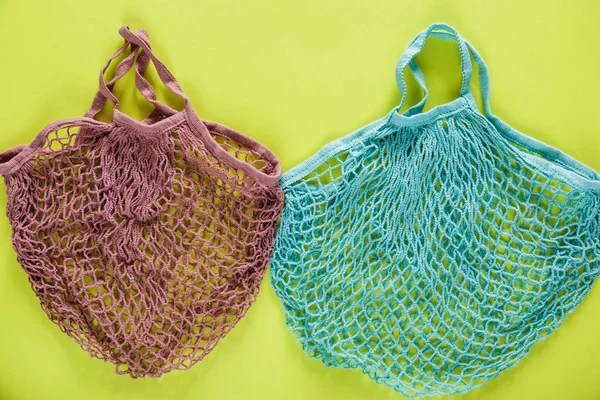 Reusable cotton mesh bags on green background.  Eco-friendly shopping bags. Close up.  Zero waste grocery concept. Sustainable lifestyle with no plastic.
