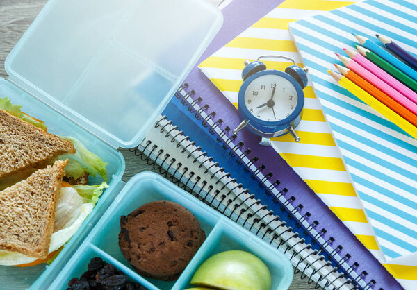 Школьная синяя обеденная коробка с домашним сэндвичем, зеленым яблоком, печеньем, карандашами, часами, блокнотами на столе. Здоровое питание в школе. Вернемся к школьному образованию. Плоский, вид сверху
.