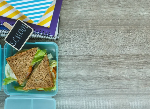 School blue lunch box with homemade sandwich,  green apple, cookies, pencils, clock, notebooks on the table. Healthy eating at school. Back to school background.  Flat lay, top view.