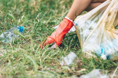 Eldivenli beyaz tişörtlü çocuk sahilde ki mavi pakette çöp ve plastik şişeleri topluyor. Genç gönüllü. Çevre koruma, çevre kavramını korumak. Eldivenle ellerinizi kapatın