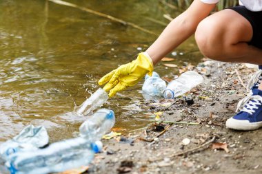 Eldivenli beyaz tişörtlü çocuk sahilde ki mavi pakette çöp ve plastik şişeleri topluyor. Genç gönüllü. Çevre koruma, çevre kavramını korumak. Eldivenle ellerinizi kapatın