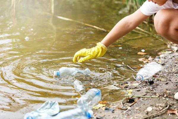 Eldivenli beyaz tişörtlü çocuk sahilde ki mavi pakette çöp ve plastik şişeleri topluyor. Genç gönüllü. Çevre koruma, çevre kavramını koruma. 