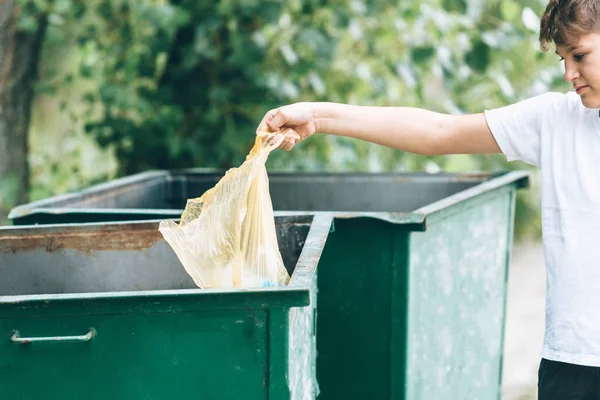 Eldivenli beyaz tişörtlü çocuk sahilde ki mavi pakette çöp ve plastik şişeleri topluyor. Genç gönüllü. Çevre koruma, çevre kavramını koruma. 