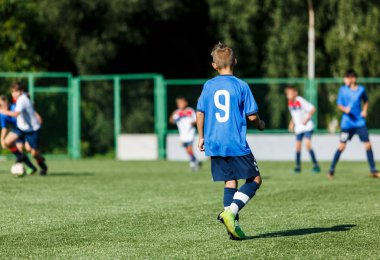 Beyaz ve mavi spor giyen çocuklar sahada futbol oynar, top top akıtır. Yeşil çimüzerinde topu ile genç futbolcular. Eğitim, futbol, çocuklar için aktif yaşam tarzı kavramı 