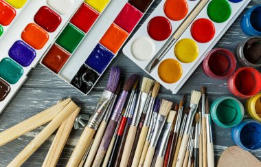 Ressam fırçalarını, paletleri ve suluboyaları grunge gri ahşap arka planda kapatın. Çok renkli boyalar seti.