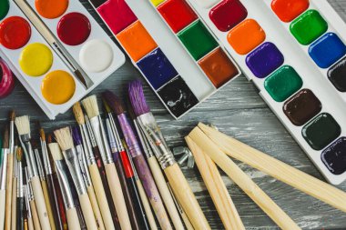 Ressam fırçalarını, paletleri ve suluboyaları grunge gri ahşap arka planda kapatın. Çok renkli boyalar seti.