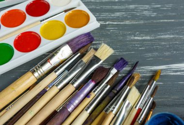 Ressam fırçalarını, paletleri ve suluboyaları grunge gri ahşap arka planda kapatın. Çok renkli boyalar seti.