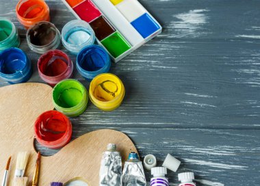 Ressam fırçalarını, paletleri ve suluboyaları grunge gri ahşap arka planda kapatın. Çok renkli boyalar seti.